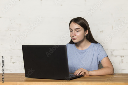 The girl works on a laptop. She's sitting at the table