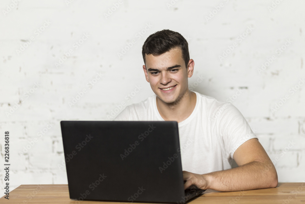 A young guy sitting at a table and working on a laptop. He's smiling. A young guy sitting at a table and working on a laptop. He's smiling.