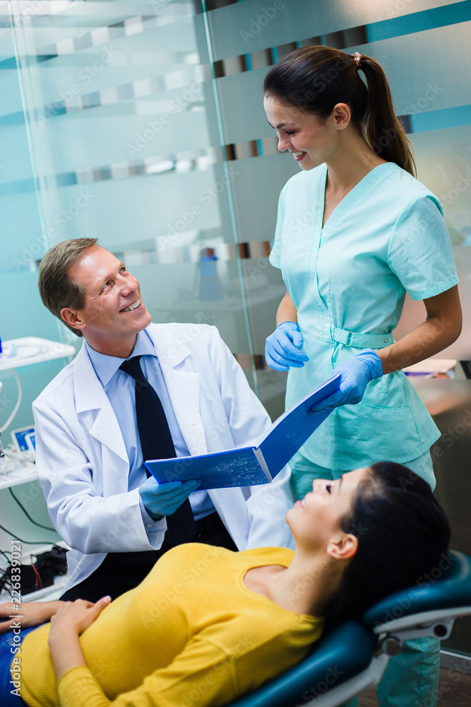 Fototapeta premium In dental office. Dentist with his assistant examining his beautiful patient in dentist’s office