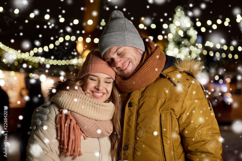 winter holidays and people concept - happy young couple dating and hugging at christmas market in evening