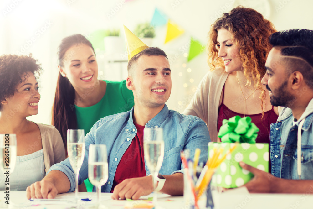 corporate, celebration and people concept - happy team with gifts and champagne glasses greeting colleague at office birthday party