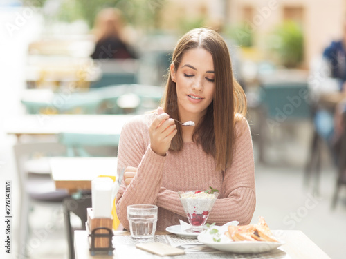 Young beautiful woman sitting in a cafe outdoors and eating salad