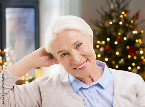 holidays, age and people concept - happy smiling senior woman at home over christmas tree lights background