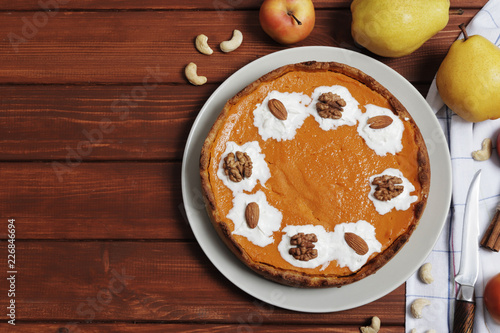 Sweet pumpkin pie close up on a brown wooden background. Pumpkin pie with whipped cream and nuts. Apples and pears. Place for text.