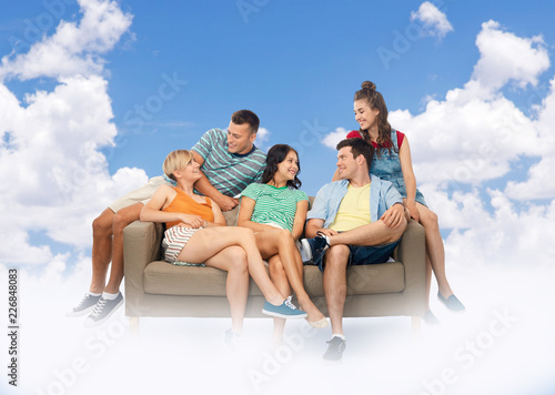 friendship, leisure and people concept - group of happy smiling friends sitting on sofa over sky and clouds background © Syda Productions