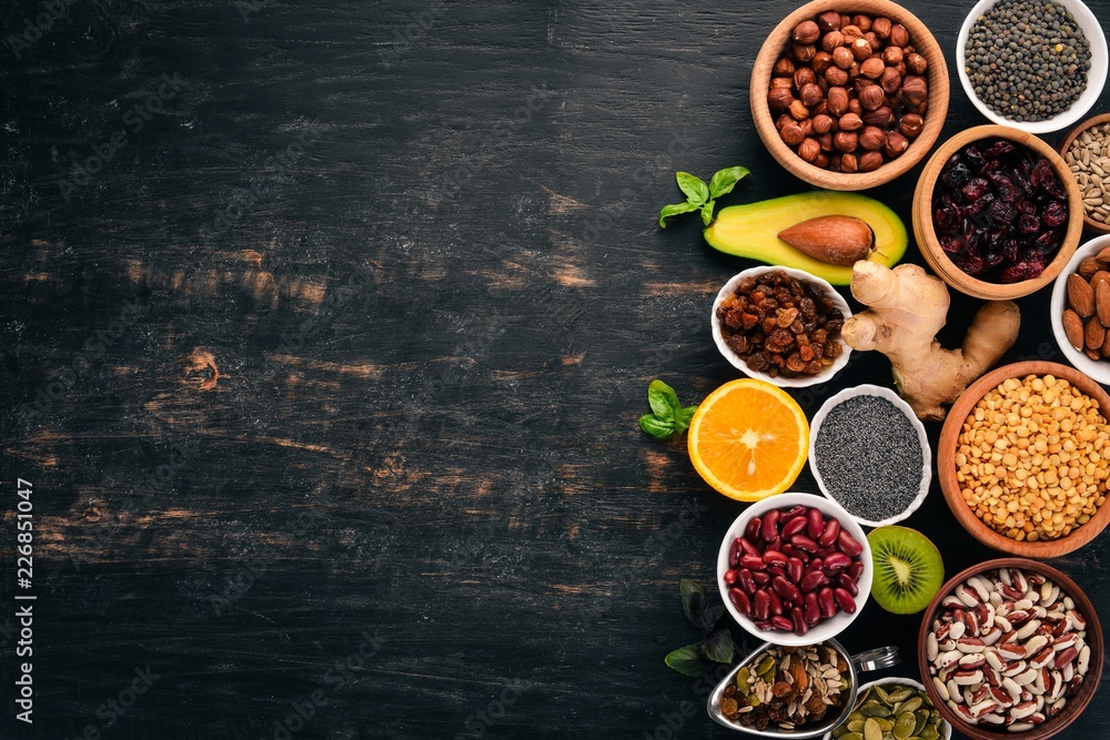 Various superfoods. Dried fruits, nuts, beans, fruits and vegetables. On a black wooden background. Top view. Free copy space.