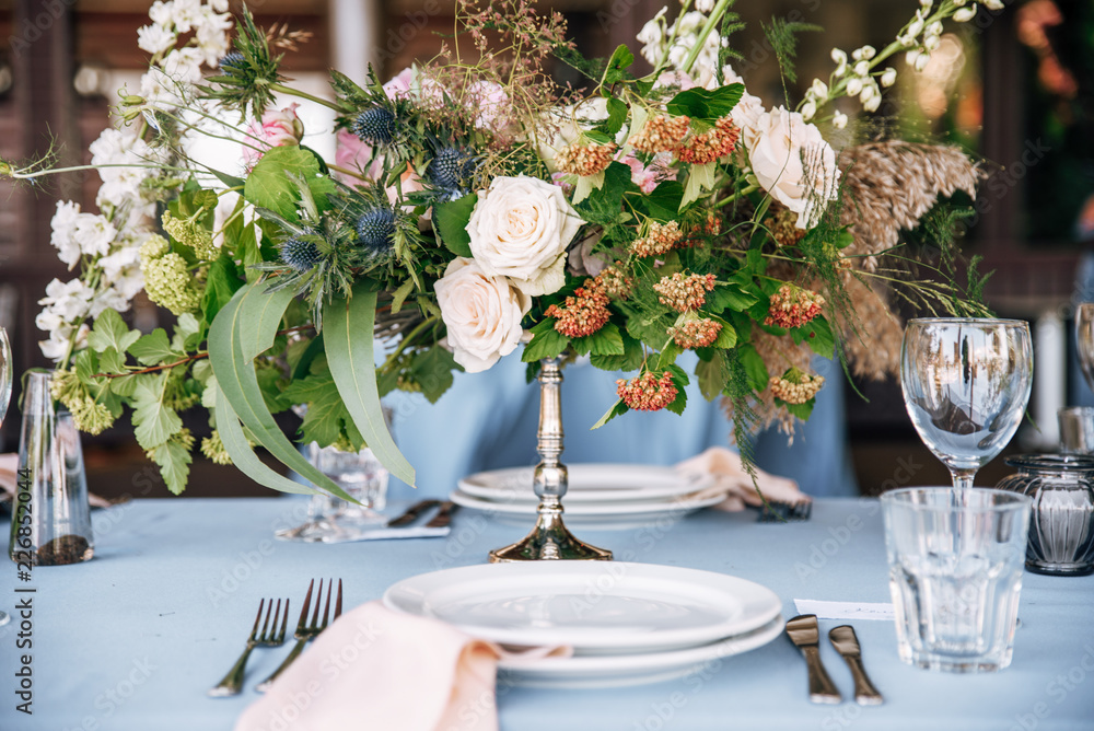 Festive table with blue tablecloth decorated with flowers in hight silver vase Festive table with blue tablecloth decorated with flowers in hight silver vase