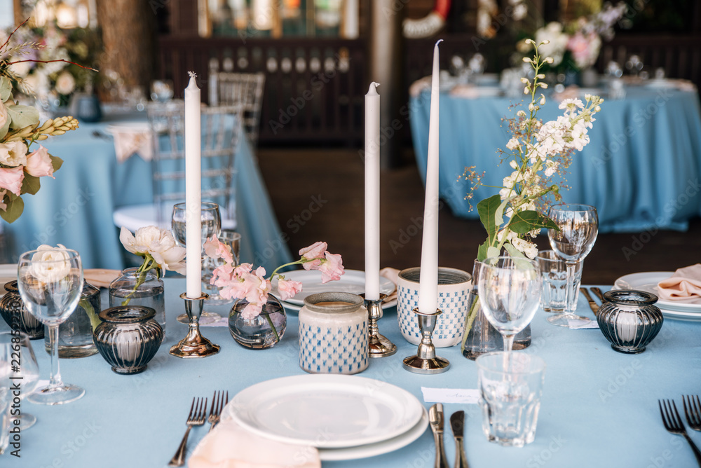 Festive table decorated with flowers and candles on a silver candlestick on blue tablecloth Festive table decorated with flowers and candles on a silver candlestick on blue tablecloth