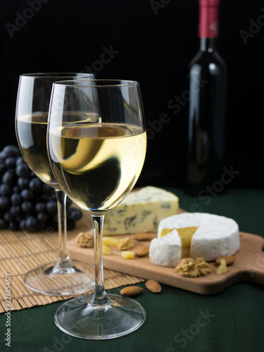 Glass of white wine, cheeses and grapes on black background