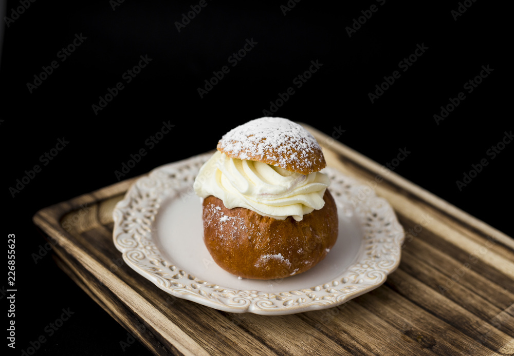 Tasty small sweet cake with whipped cream and powdered sugar on top on a wooden tray, black background. Tasty small sweet cake with whipped cream and powdered sugar on top on a wooden tray, black background.