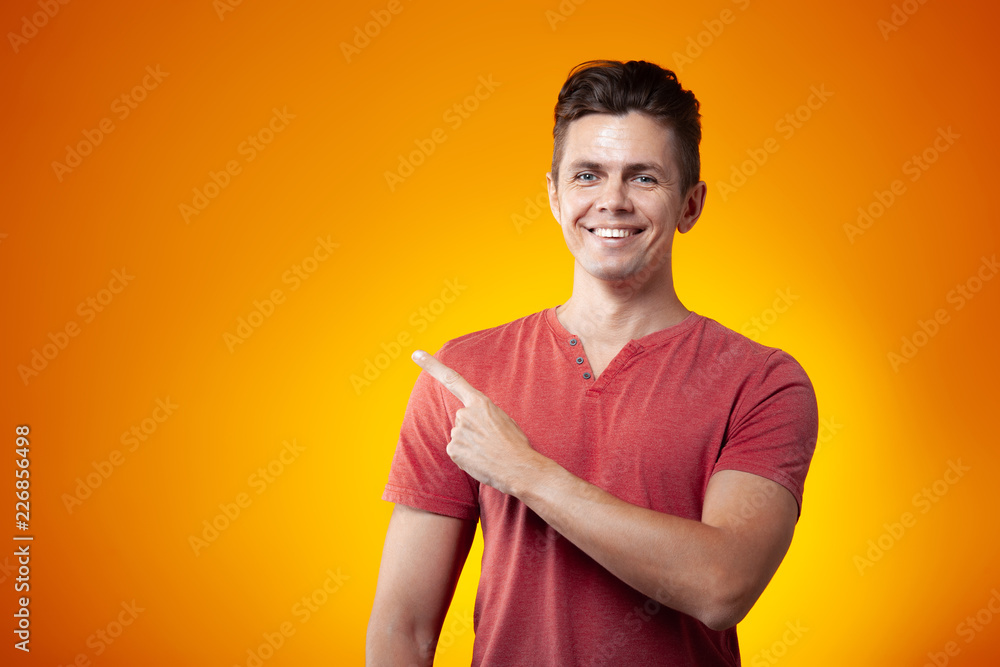 Adult cheerful man smiling and points with finger on an orange background Adult cheerful man smiling and points with finger on an orange background