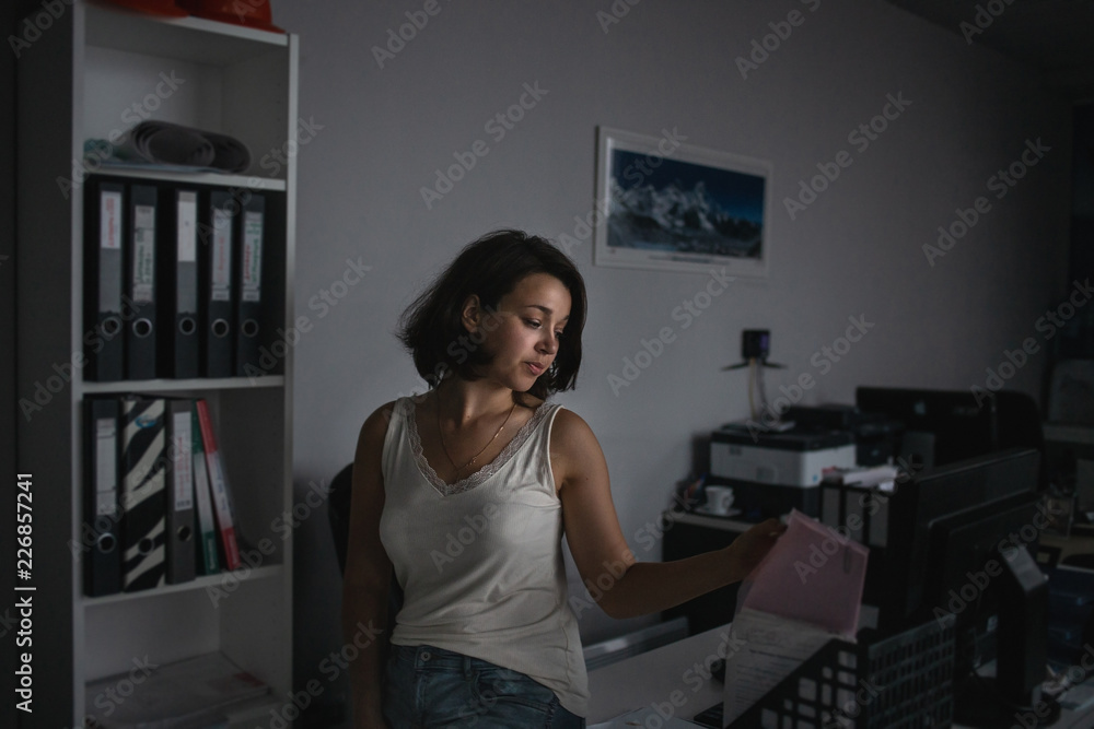 Atmospheric portrait of young seductiveworker holding docs at her workplace in evening. Overtime work concept