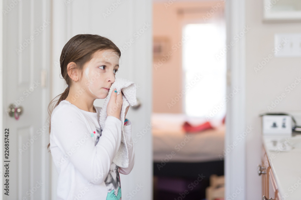 Side view of a young girl cleaning her face with a washcloth Side view of a young girl cleaning her face with a washcloth