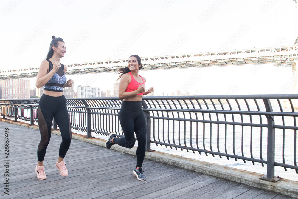 Two women running  together outside on a pier near water
