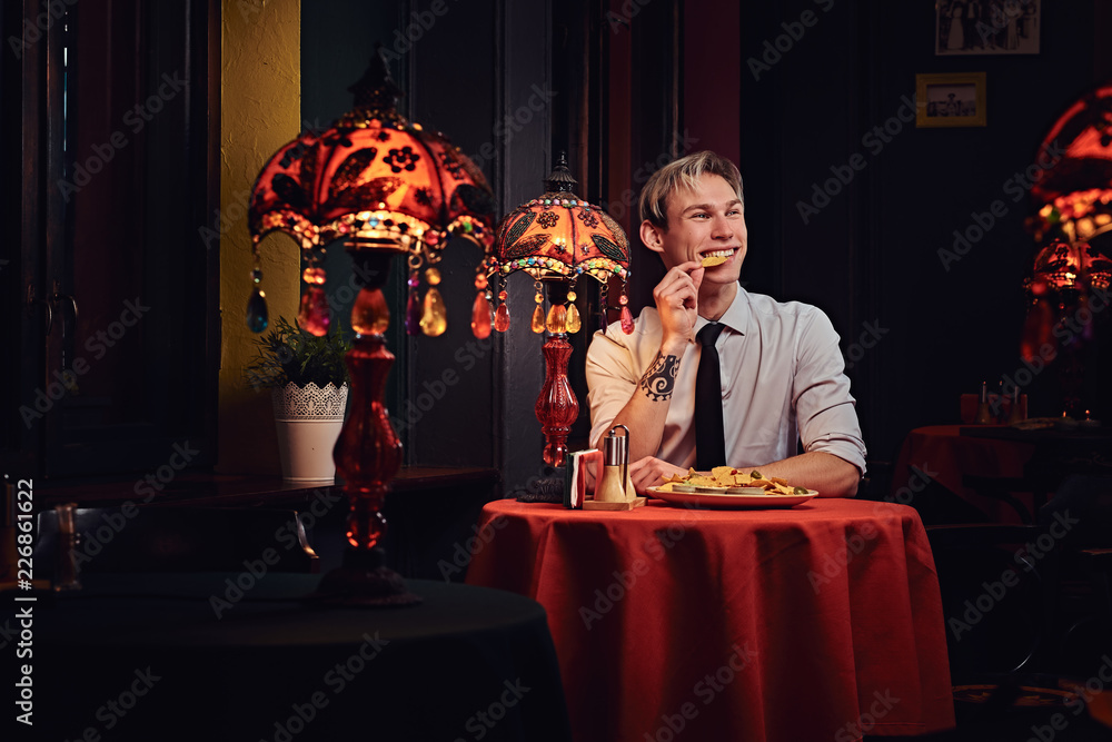 Handsome young man in white shirt and tie eating nachos at mexican restaurant. Handsome young man in white shirt and tie eating nachos at mexican restaurant.