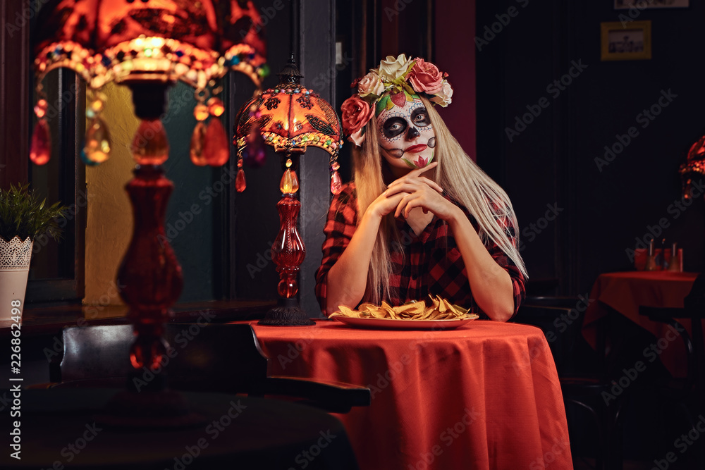 Young blonde girl with undead makeup in flower wreath eating nachos at a mexican restaurant.