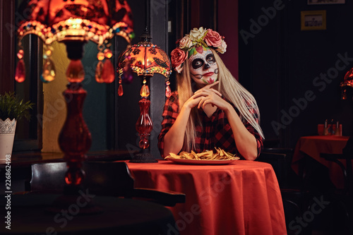 Young blonde girl with undead makeup in flower wreath eating nachos at a mexican restaurant.