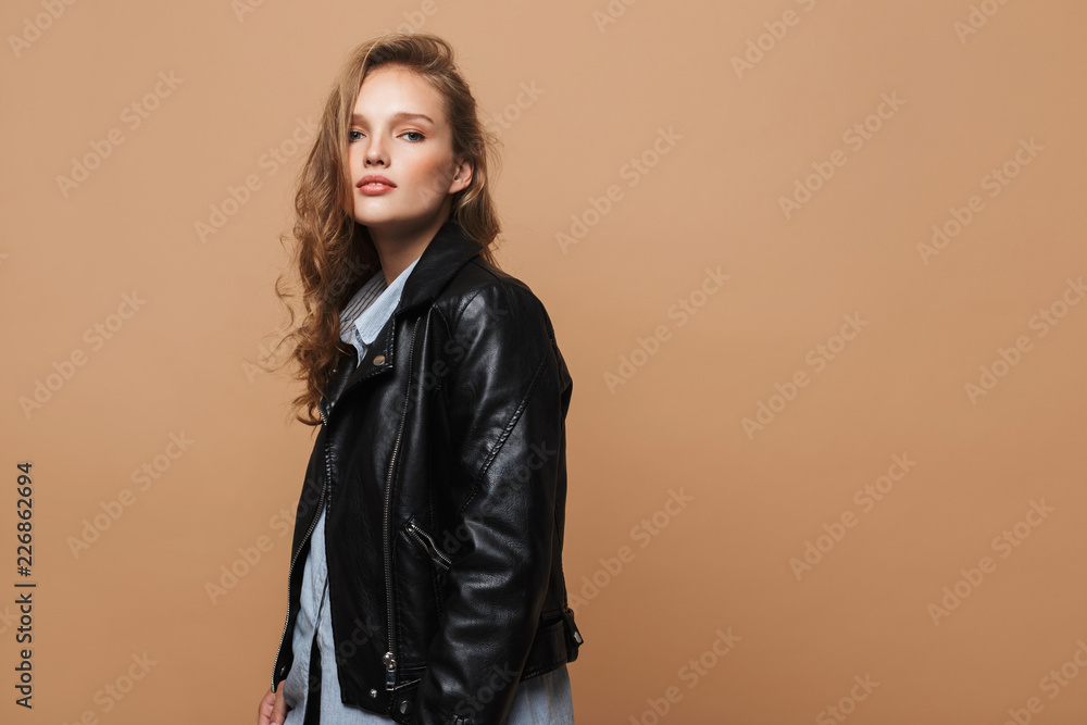 Beautiful girl with wavy hair in black leather jacket and shirt dreamily looking in camera over beige background isolated Beautiful girl with wavy hair in black leather jacket and shirt dreamily looking in camera over beige background isolated