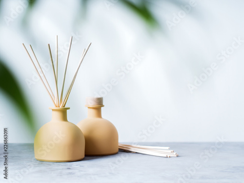 aroma reed diffuser home fragrance with rattan sticks on a light background with palm leaves and shadows.