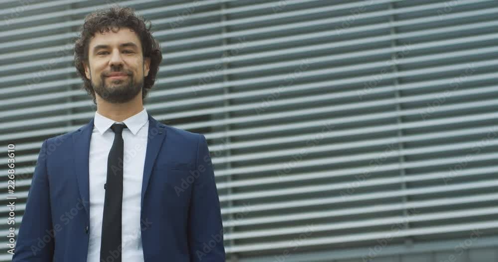 Portrait shot of the attractive young Caucasian businessman in the suit and tie looking at the side and then smiling to the camera. Outside. Portrait shot of the attractive young Caucasian businessman in the suit and tie looking at the side and then smiling to the camera. Outside.
