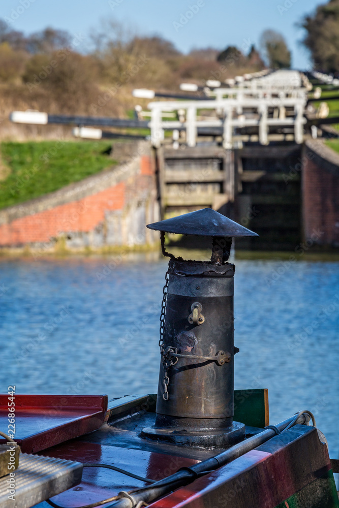 Close up of canal boat iron chimney with flight of locks in background