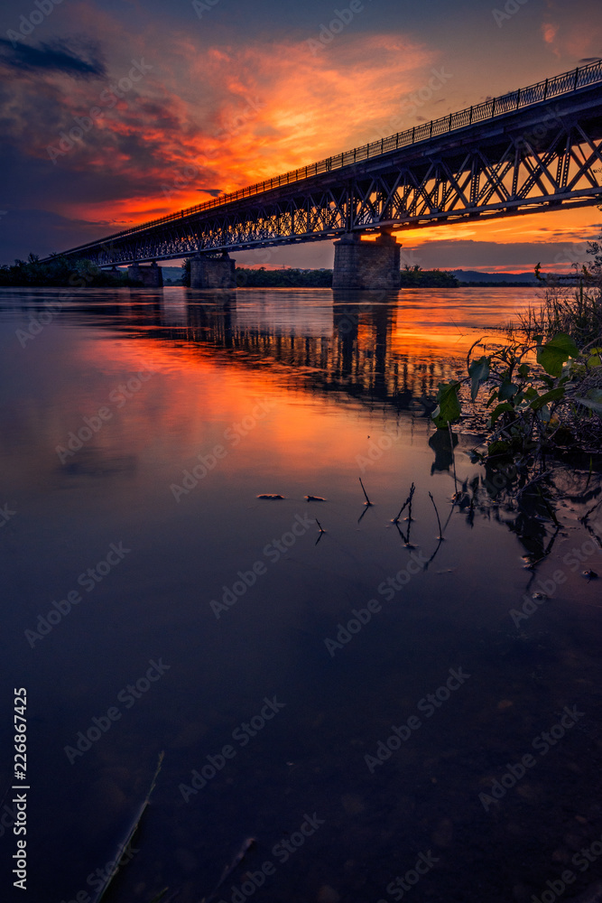 Road bridge crossing a river at sunset with beautiful clouds on sky