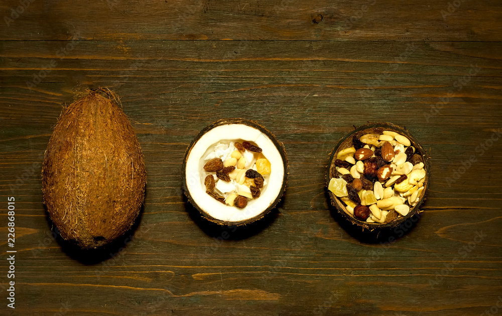 Vegetarian salad with coconut shavings and nuts in coconut bowl on wooden background. The concept of  tasty and healthy meal, copy space, closeup.Flat lay.