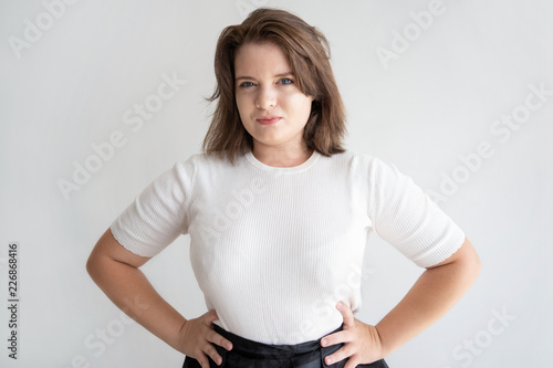 Smiling chubby girl posing in studio. Portrait of confident young woman standing with hands on her hips.  Beauty concept