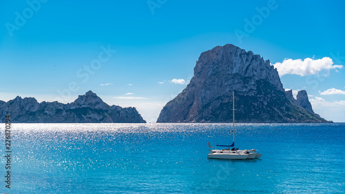 Ibiza, Cala d’Hort beach, beautiful sunny seascape with a sailboat and rocks in the sea 