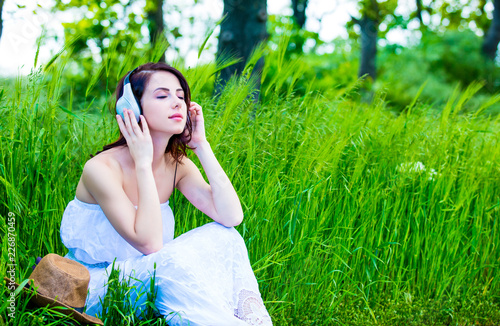 portrait of the beautiful young woman with earphones sitting in the field