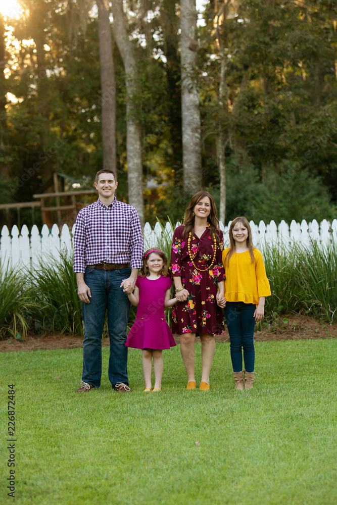 Obraz premium Family of Four Holding Hands Outside of Home with White Picket Fence
