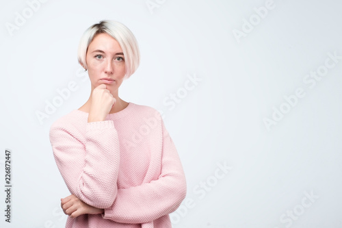 Thoughtful model with short dyed hair dressed in pink sweater standing in studio. photo