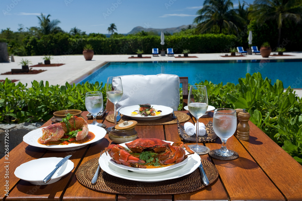 Luxury, romantic, poolside restaurant, table set for two with gourmet crustaceans, fish, salad and wine