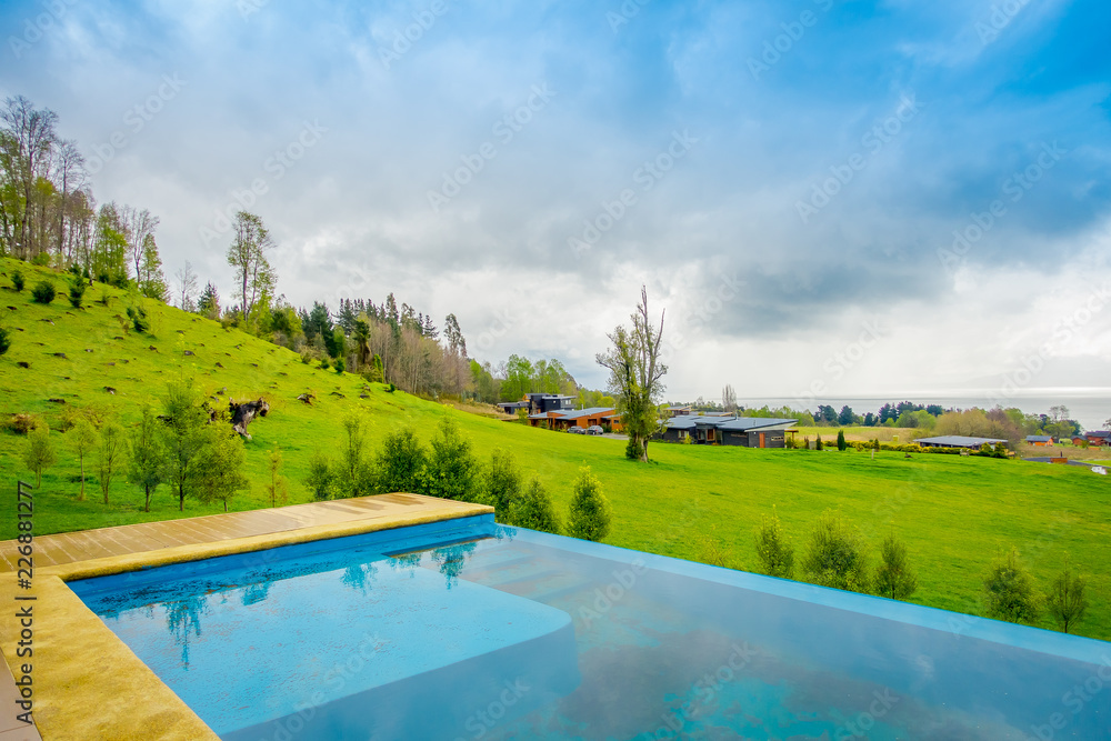 Beautiful outdoor view of infinity swimming pool with a gorgoues green grassland and lake in the horizont located at Pucon city, Chile