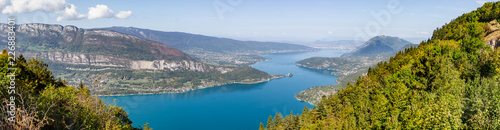 Panoramic view from Lake Annecy in Haute Savoie, France. The turquoise lake is lit by the sun. Some boats are travelling on the water.
