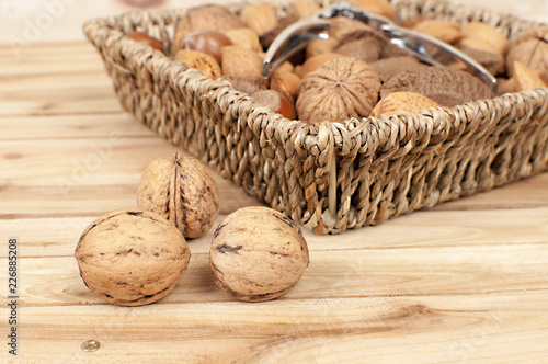 different kind of nuts in straw basket on wooden table with nutcracker