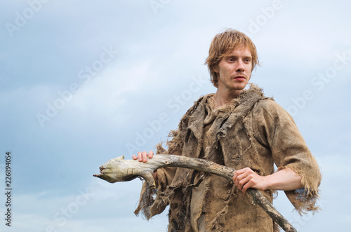 young shaman with a staff of an old stick on the background of a blue sky peering into the distance