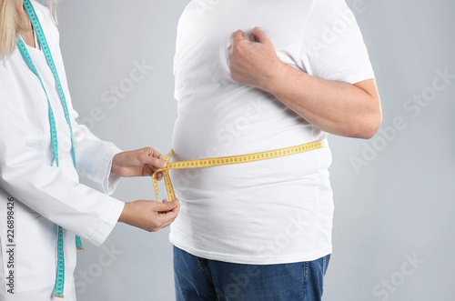 Doctor measuring senior man's waist on grey background. Weight loss