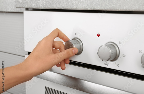 Woman adjusting electric oven in kitchen, closeup