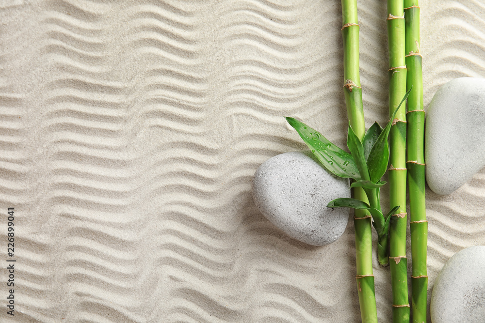 Fototapeta premium Bamboo branches with spa stones on sand, top view. Space for text
