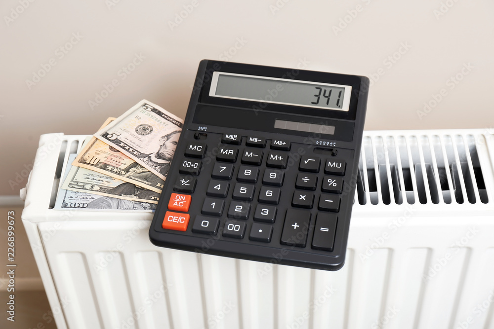 Calculator and money on heating radiator indoors Calculator and money on heating radiator indoors