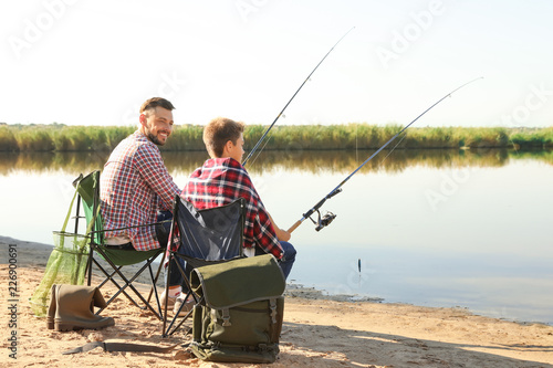 Father and son fishing together from riverside on sunny day