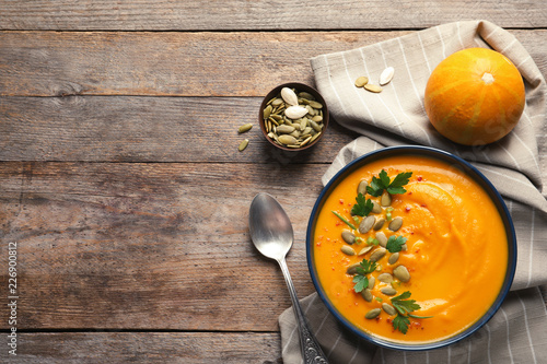 Flat lay composition with pumpkin cream soup in bowl on wooden background. Space for text