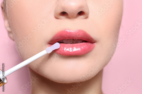 Beautiful young woman applying gloss on her perfect lips, closeup photo