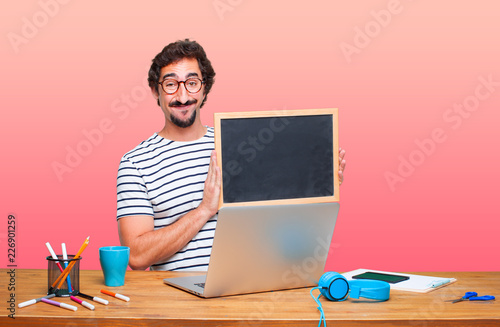 young crazy graphic designer on a desk with a laptop and with a placard photo