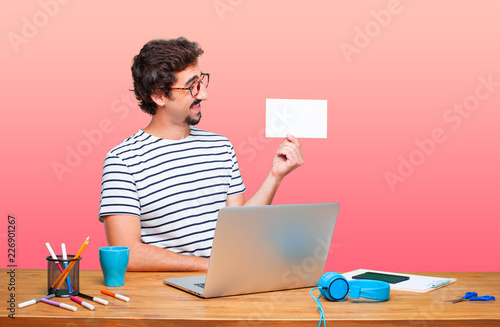 young crazy graphic designer on a desk with a laptop and with a placard photo