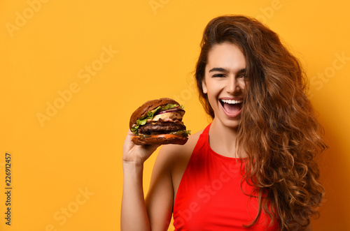 Woman hold big barbecue burger sandwich with hungry mouth happy screaming laughing on yellow background