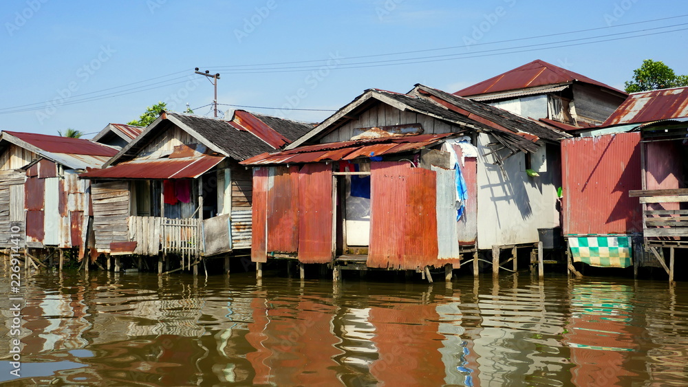 einfache Hütten in Borneo stehen auf Stelzen im Fluss Martapura und spiegeln sich im Wasser 