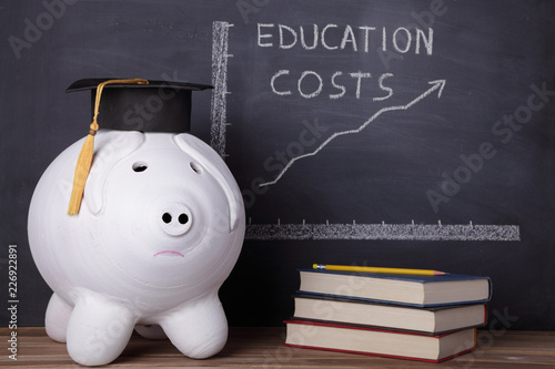 Photos Big piggy bank with graduation cap is standing next to an education chart that i