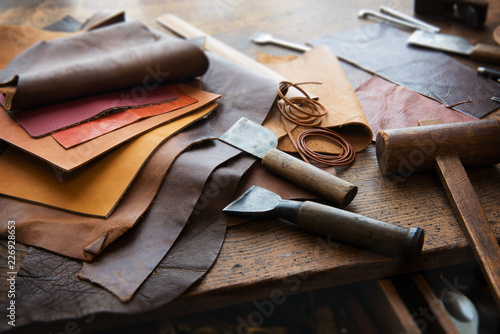 Leather craft or leather working. Selected pieces of beautifully colored or tanned leather on leather craftman's work desk . Piece of hide and working tools on a work table.